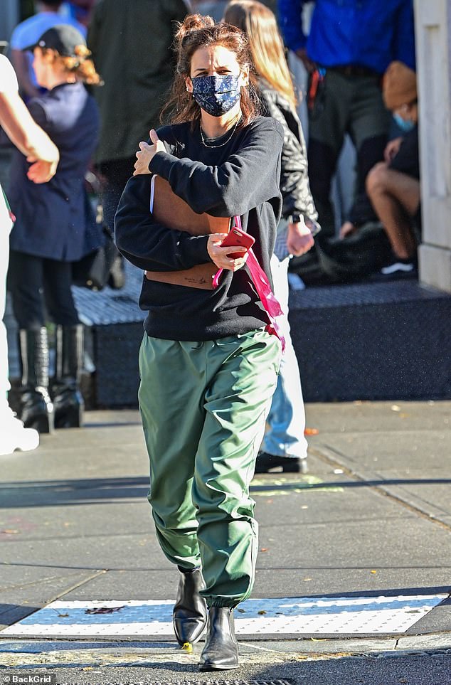 Katie Holmes holds a notebook close to her chest as she wears baggy pants