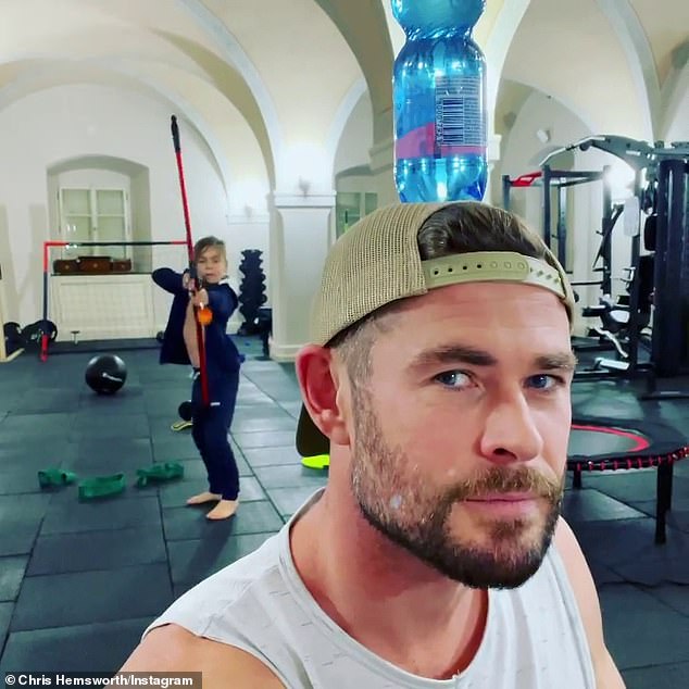 Chris Hemsworth laughs as his son expertly shoots a water bottle off his head with rubber arrow