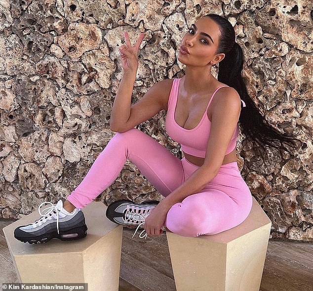 Kim Kardashian flashes a peace sign while in a pink bra top and leggings