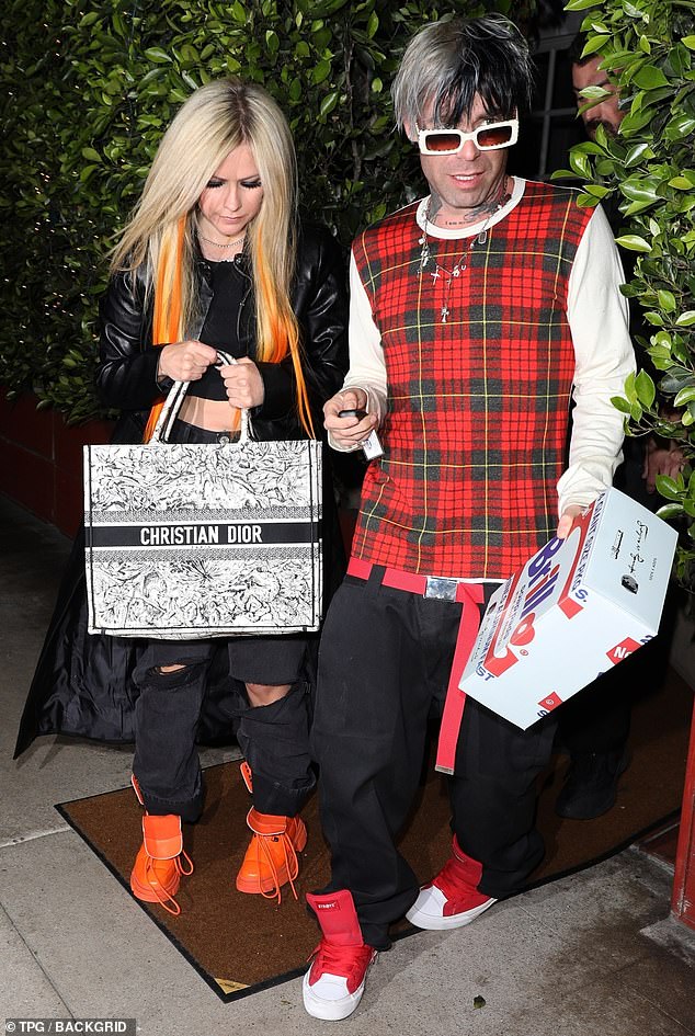 Avril Lavigne flashes her toned midriff in a black crop and matches orange trainers to neon hair