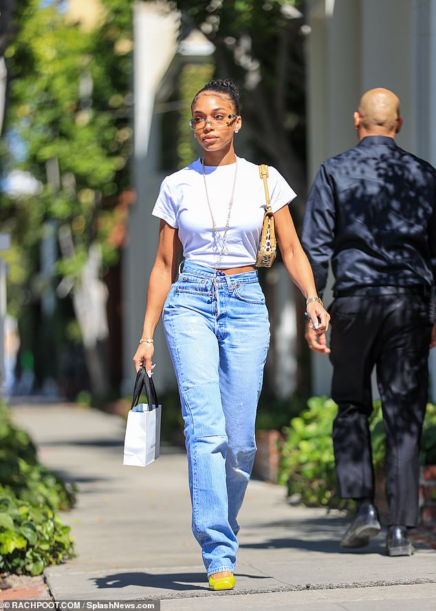 Lori Harvey shows a hint of her toned midriff in a white crop top and jeans